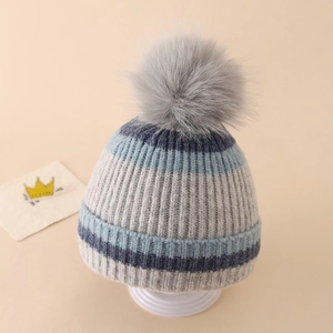 Close-up of winter knit hat featuring grey and blue stripes and a fluffy pom-pom top