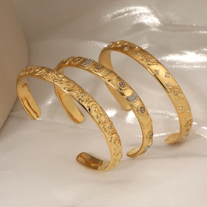 Three gold stainless steel open bangles with celestial patterns and zircons on silk