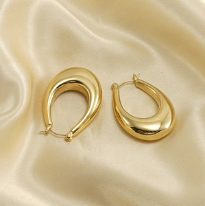 Macro detail of high-polish 18K gold waterdrop earrings on champagne satin fabric