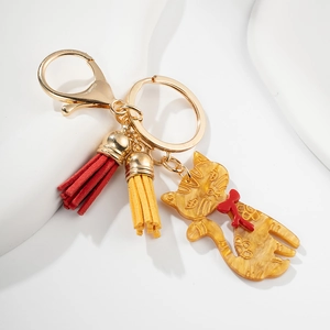 Detail of yellow amber texture cat keychain with red bow and suede tassels on white base