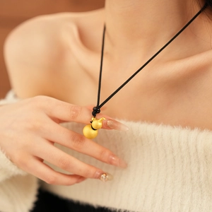 Detail of a brushed gold gourd pendant necklace on a model wearing a beige sweater