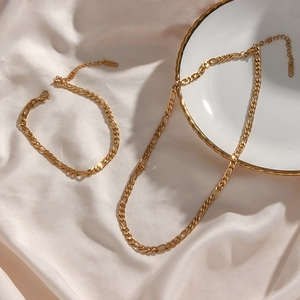 Detailed view of golden Figaro chain necklace and bracelet set on a silk and ceramic plate