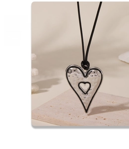 Macro shot of silver hammer-textured heart pendant with black cord on beige background