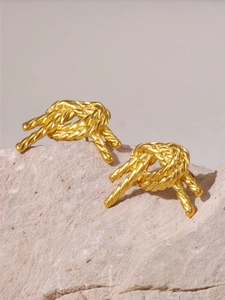 Gros plan de boucles d'oreilles nœuds dorées sur un support en pierre texturé