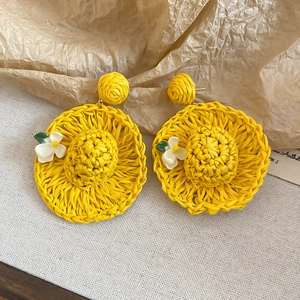 Macro shot of handmade yellow raffia straw hat earrings with small floral details