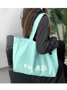 Detail of mint green canvas tote bag featuring white voyage lettering for travel