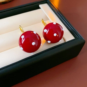 Detailed view of Ancora red spherical earrings with white polka dots on a beige cushion