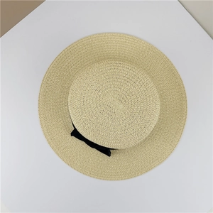 Détail d'un chapeau de paille beige tissé avec ruban noir sur un fond de style minimaliste