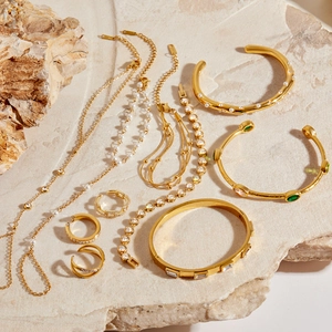 Détails de bijoux dorés avec perles et pierres vertes posés sur pierre naturelle