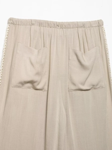 Detail view of beige wide-leg pants with elastic waist and white lace side trim