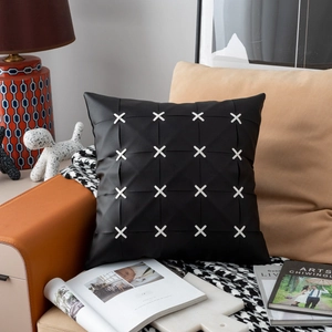 Detail of a black leather pillow cover with white cross-weave patterns on a modern sofa