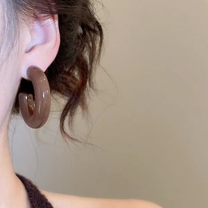 Close-up of a glossy brown acrylic C-shaped hoop earring worn by a model in soft light