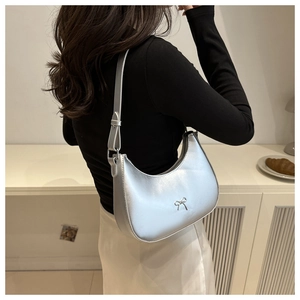 Silver bow-accented crescent shoulder bag on model in a minimalist room setting