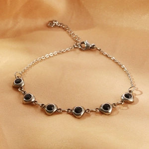 Detailed view of silver stainless steel bracelet with six black heart-shaped zircons on silk