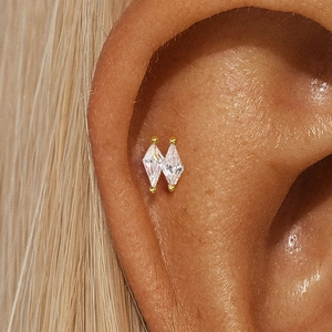 Close-up of gold cartilage piercing featuring two vertical diamond-shaped clear crystals