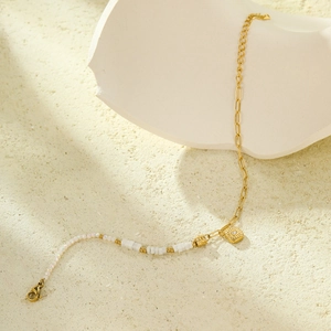 Detail of beaded bracelet featuring a gold sun pendant and square white beads on stone