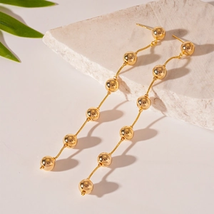 Detailed close-up of golden beaded tassel earrings on natural stone with leaf accents