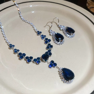 Detail of dark blue teardrop zircon pendant necklace and earrings on ceramic tray