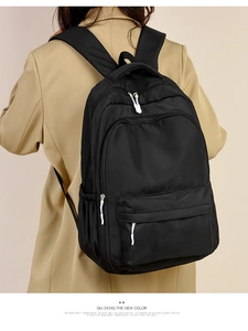 Detail view of a black nylon backpack with multi-layer zipper pockets worn by a model