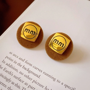 Detail of square gold metal and brown flocked resin earrings on a vintage book page