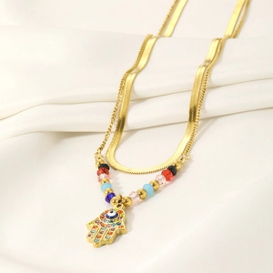 Detailed macro view of gold double-layer necklace with Hamsa Hand and Evil Eye pendant