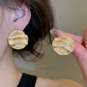 Détail macro de grandes boucles d'oreilles dorées avec texture ondulée irrégulière