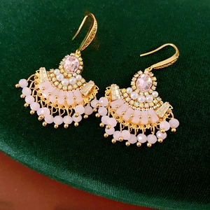 Détail de boucles d'oreilles dorées en éventail avec gemmes roses et perles sur velours