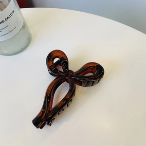 Detail of an amber bow-shaped plastic hair claw clip on a clean white surface