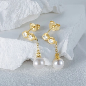 Macro shot of gold S925 silver earrings with zircons and pearls on white stones