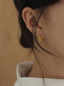 Close-up of golden twisted hoop earrings on a model with warm yellow lighting