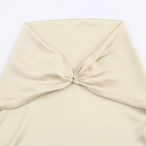 Top a fascia asimmetrico in raso beige con dettaglio a pieghe intrecciate su sfondo bianco