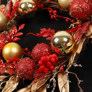 Red and gold Christmas wreath with glitter ornaments and berries on black background