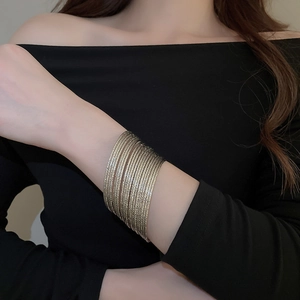 Detail of stacked gold bangle set featuring 15 textured rings on model wrist