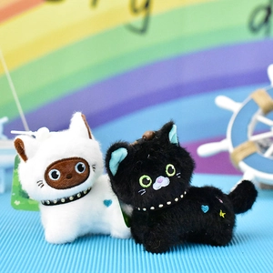 Close-up of two cute plush cat charms in black and white with heart details.