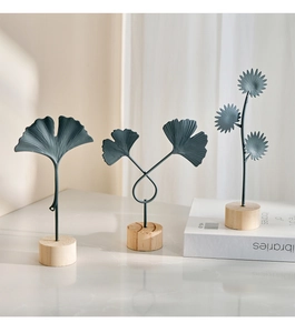 Detailed view of matte dark blue iron ginkgo leaf sculptures on cylindrical wooden bases