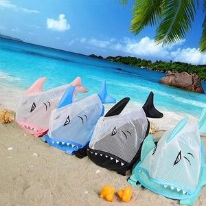 Set of four colorful shark-shaped mesh beach bags for kids on a tropical sandy shore