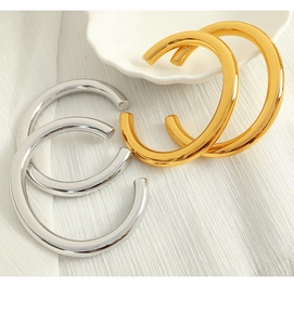 Close-up of shiny gold and silver wide C-shape hoop earrings on a white cloth background