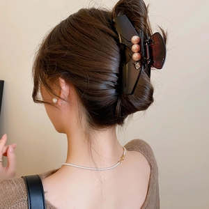 Detail of a large amber resin hair claw clip with pink gold pearls on brown hair