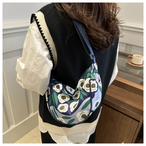 Blue floral print nylon dumpling bag with adjustable strap worn on person for scale