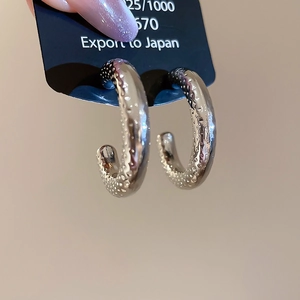 Macro detail of silver C-shaped hoop earrings with hammered textured metal surface