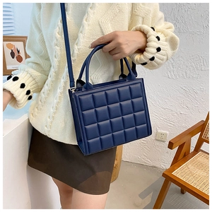 Detail of dark blue quilted handbag showing 3D checkered texture and gold hardware