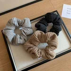 Trois chouchous tricotés en gris, noir et beige sur un plateau en bois style rétro