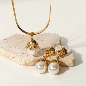 Baroque pearl pendant necklace and earrings set on a natural beige stone surface