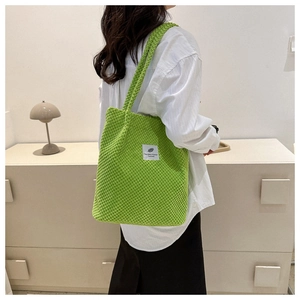 Green corduroy bucket bag with shoulder strap and stylish text label worn by model