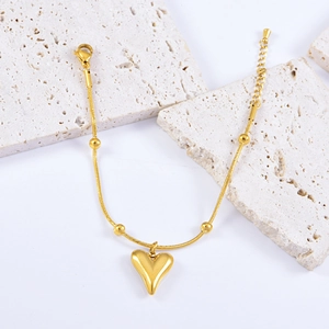Elegant gold snake chain bracelet with heart pendant and beads on a stone background