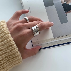 Close-up of minimalist wide irregular silver rings worn with a cream knit sweater