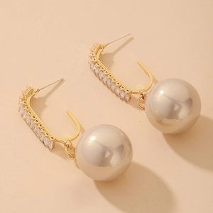 Detail of C-shaped gold earrings with sparkling cubic zirconia and baroque faux pearl drops