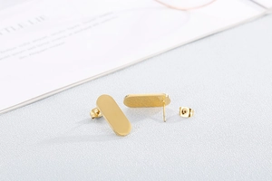 Detail of gold rectangular stud earrings with polished finish on a white textured background