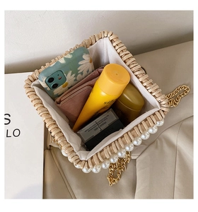 Macro view of woven straw bag interior with pearl trim and gold chain strap detail