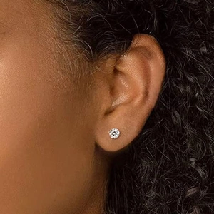 Close-up of classic round-cut diamond stud earring worn on a model with silver prongs